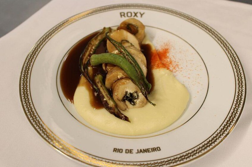 Un plato de comida con champiñones y judías verdes, adornado con una especia roja, sobre un plato blanco con borde dorado. 2