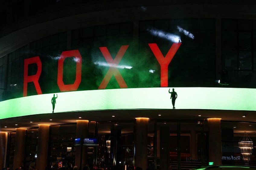 En byggnad med en upplyst skylt som visar texten ”ROXY” och två silhuettliknande figurer på taket. 2