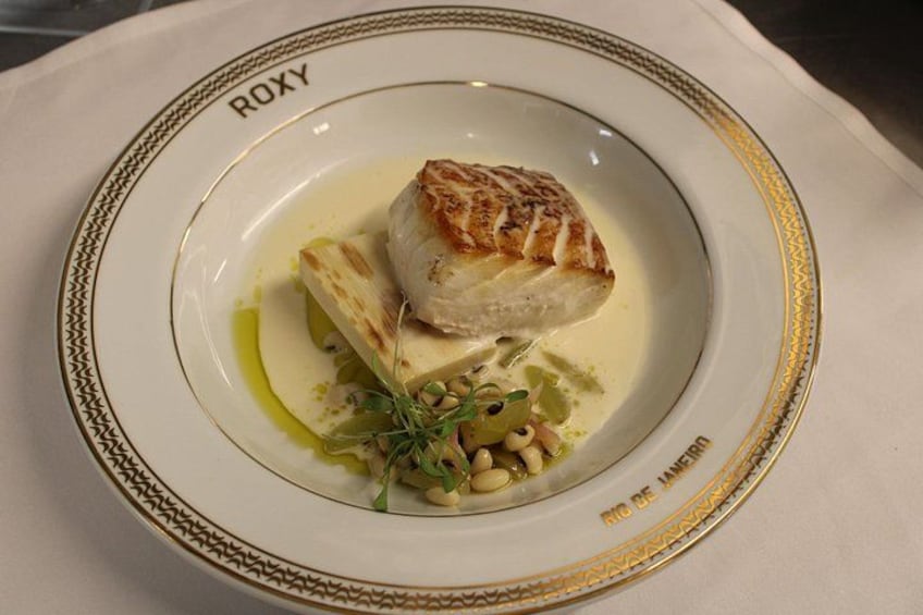 Un plato de comida con pescado y verduras sobre un plato blanco con un borde dorado. 3