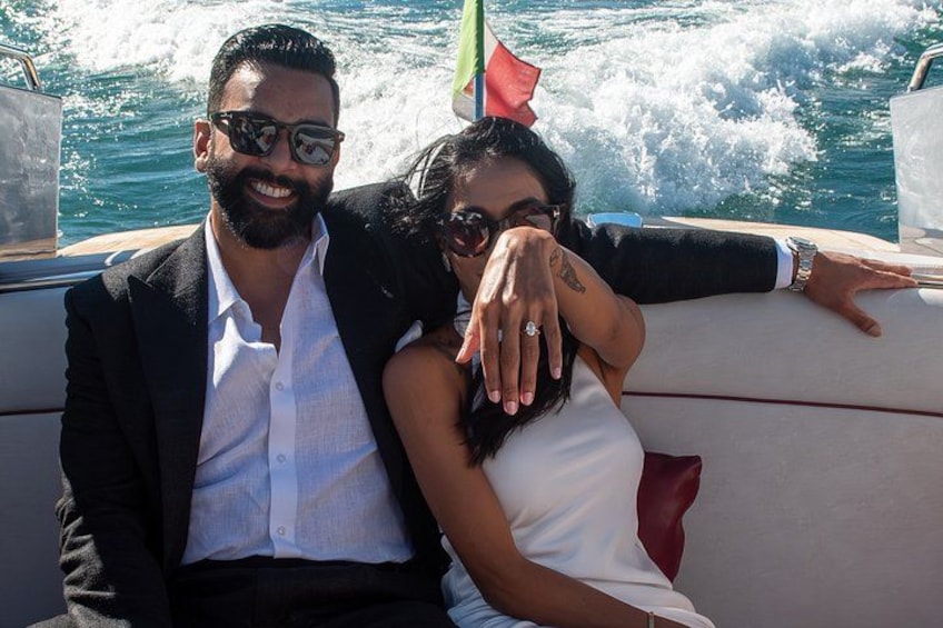 A man and a woman on a boat with a flag, water, and a red cushion. 4