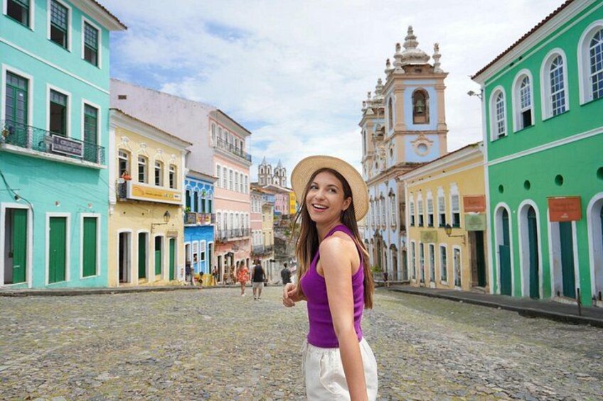 A cobblestone street lined with colorful buildings, a person in a purple top and white skirt, and a historic church in the background. 5
