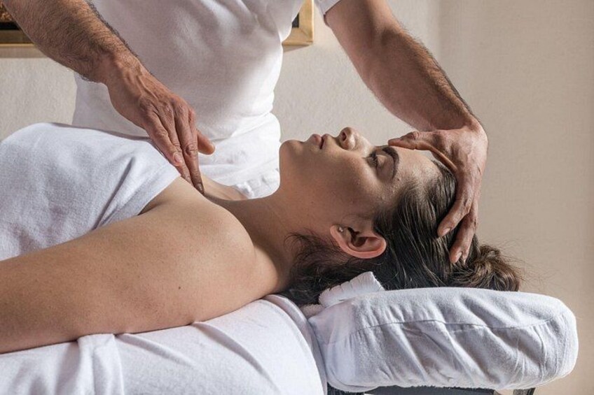 En person får massage, och massören använder händerna på personens huvud och nacke. 2