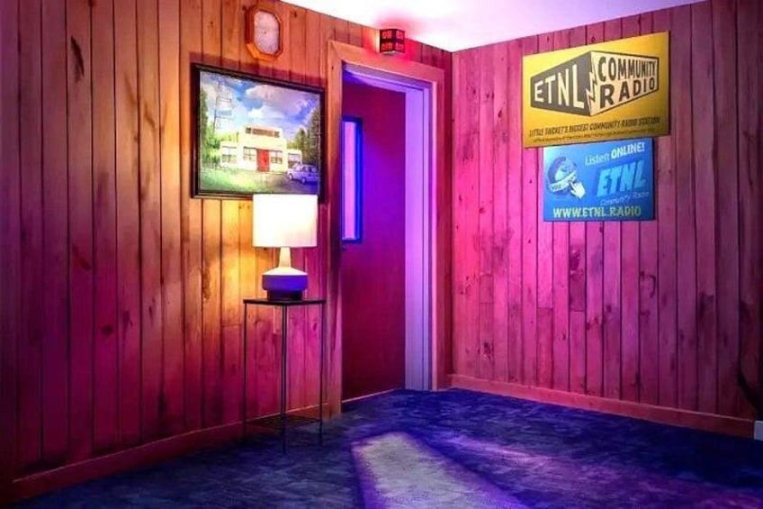 A wooden interior with a door, a framed picture, a lamp, and ETNL Community Radio signs. 4
