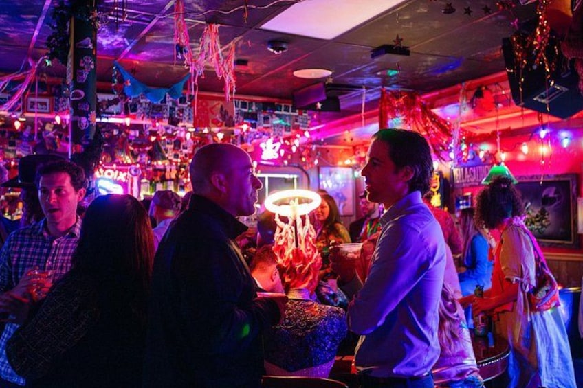 A crowded bar with neon lights and people socializing. 2
