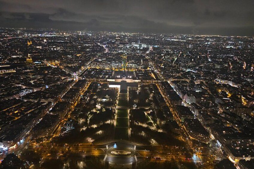 A nighttime aerial view of a city with illuminated streets and a prominent central square. 2