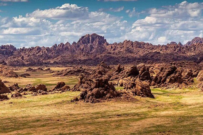A rugged landscape with rocky formations and a distant mountain range under a partly cloudy sky. 4