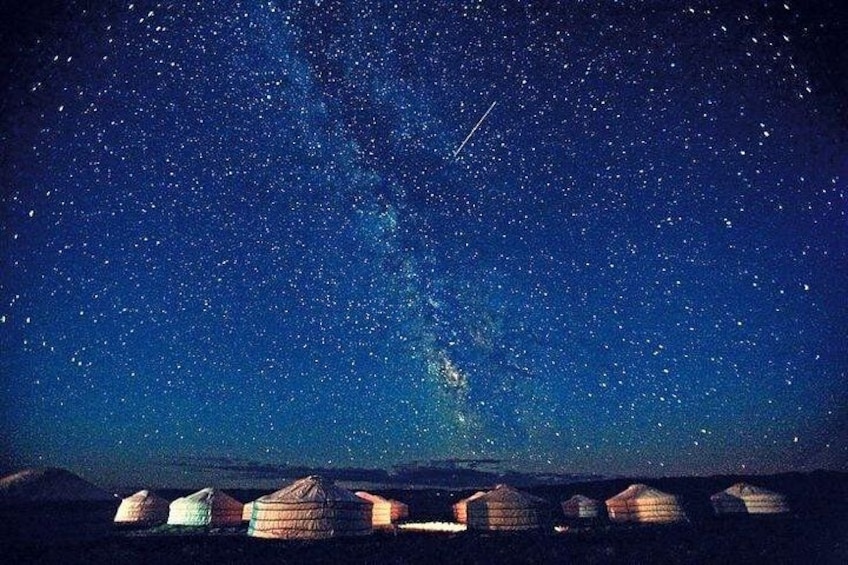 A starry night sky with the Milky Way visible, yurts in the foreground, and a mountainous landscape. 5