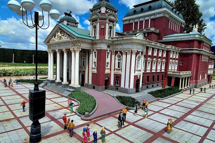 A large red building with columns and a dome, surrounded by a square plaza with people walking. 4