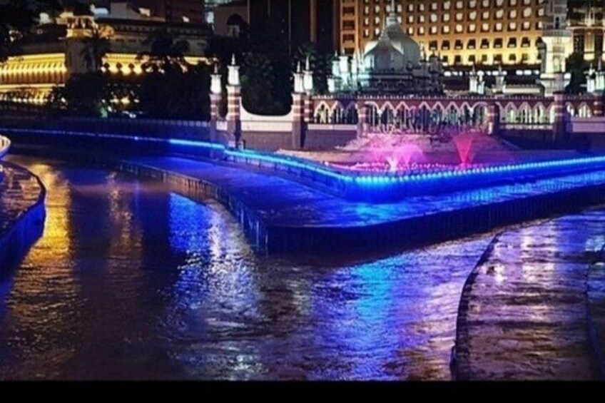A nighttime view of a water fountain with illuminated edges, a domed building in the background, and a bridge. 2
