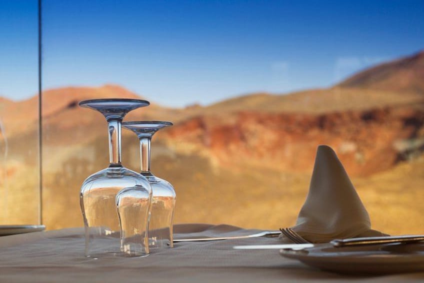 A table with two wine glasses and a cone-shaped dessert, set against a desert landscape. 4