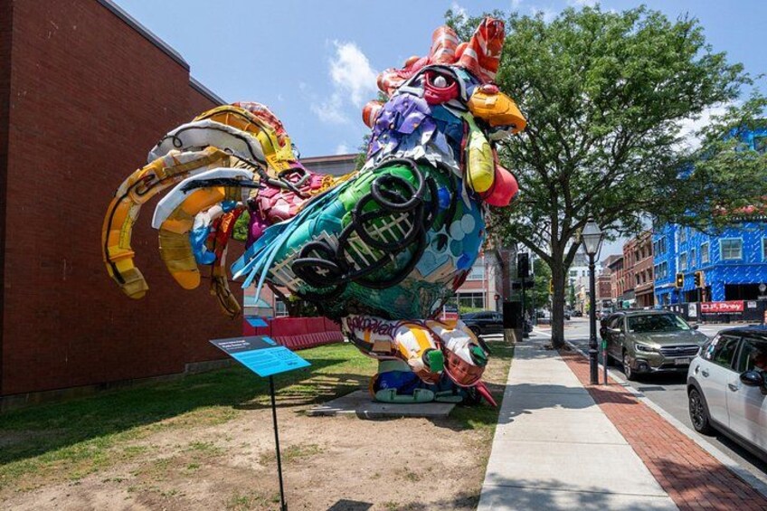 A colorful, oversized sculpture of a rooster on a sidewalk. 2