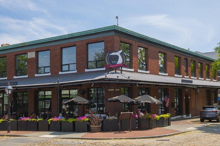 A brick building with a green roof, outdoor seating, and a sign with a bird logo. 3