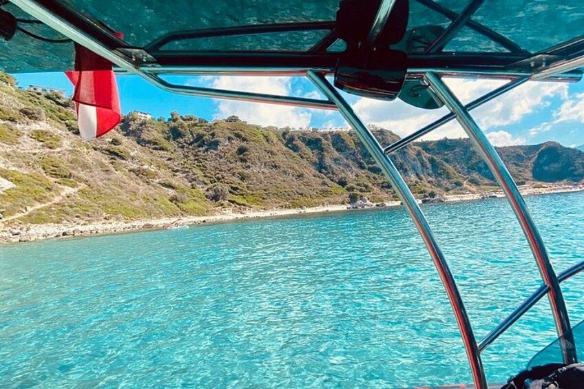 A boat on clear turquoise water with a mountainous coastline in the background. 3