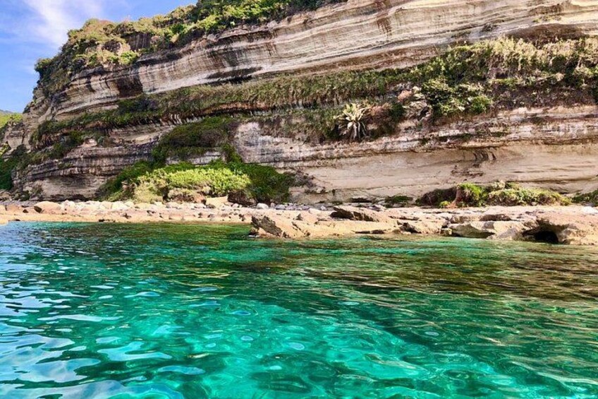 A coastal landscape with clear turquoise water, rocky cliffs, and sparse vegetation. 2