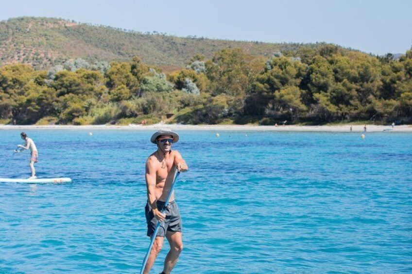 A person paddleboarding on a calm sea with a forested hill in the background. 1