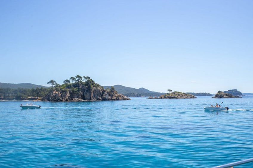 A calm sea with boats, a rocky island with trees, and distant hills. 5