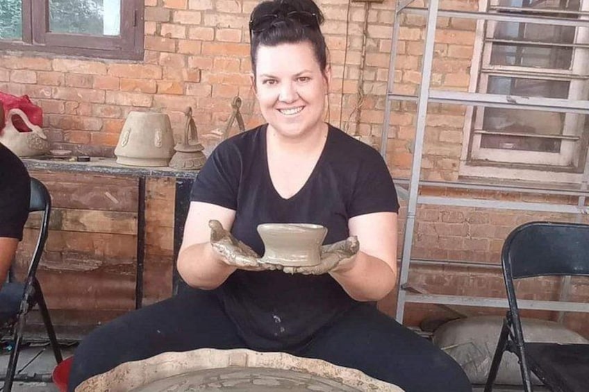 A person sitting on a chair, holding a clay pot. 2