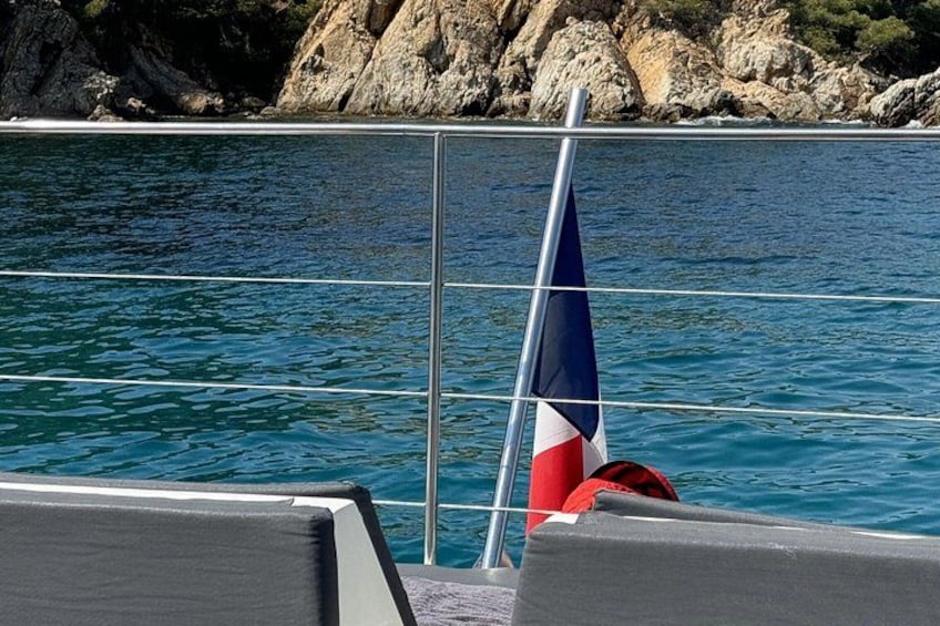 A sailboat with a blue and red sail, calm water, and rocky coastline. 2