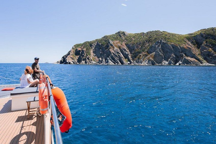A boat on the water with people on deck, a lifebuoy, and rocky cliffs in the background. 1