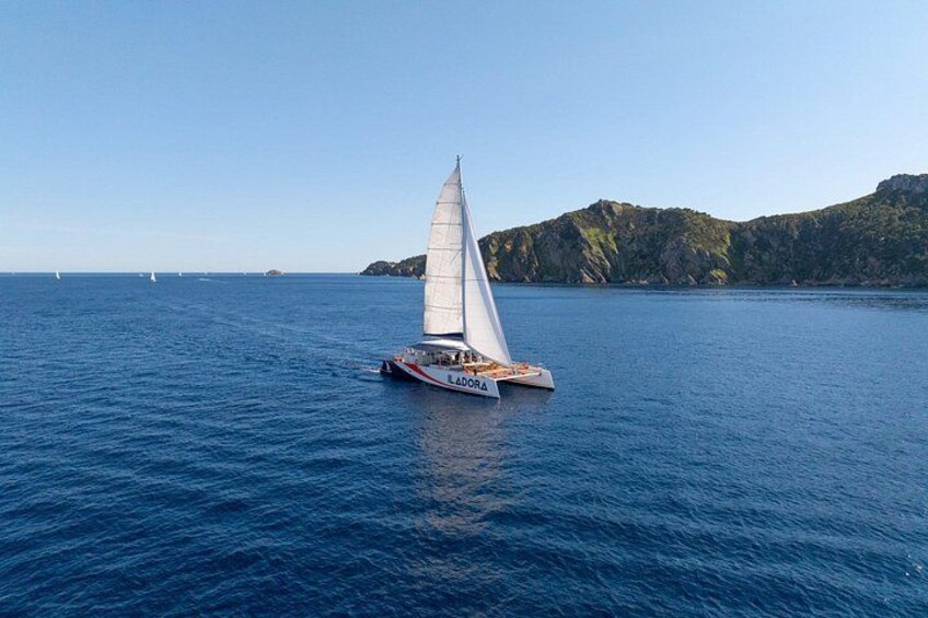 A sailboat named 'LA DORA' on calm blue waters with a rocky coastline in the background. 4