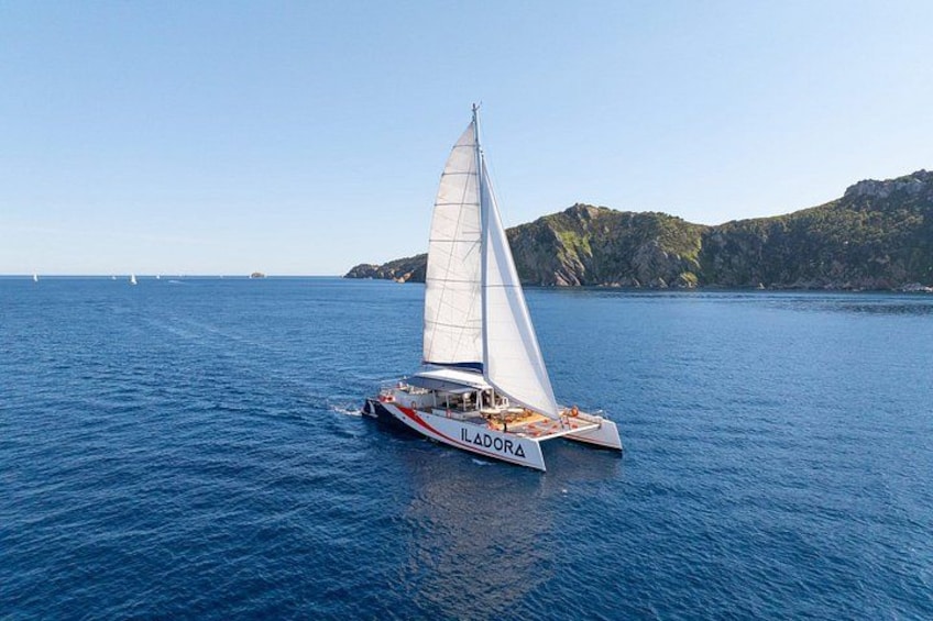 A sailboat named 'LADORA' on a calm sea with a mountainous coastline in the background. 3