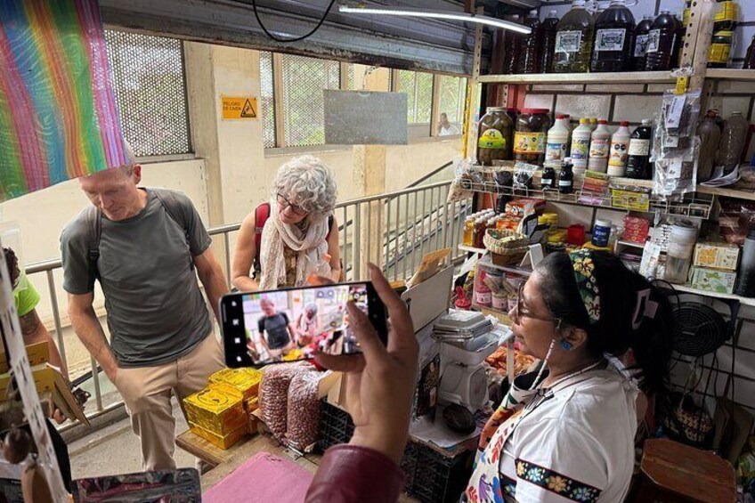 A person taking a photo of a market scene with various food items and shelves stocked with goods. 5