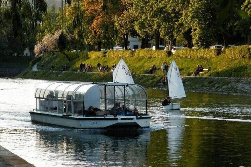 A covered boat with passengers, sailing on a river with a grassy bank and trees in the background. 3