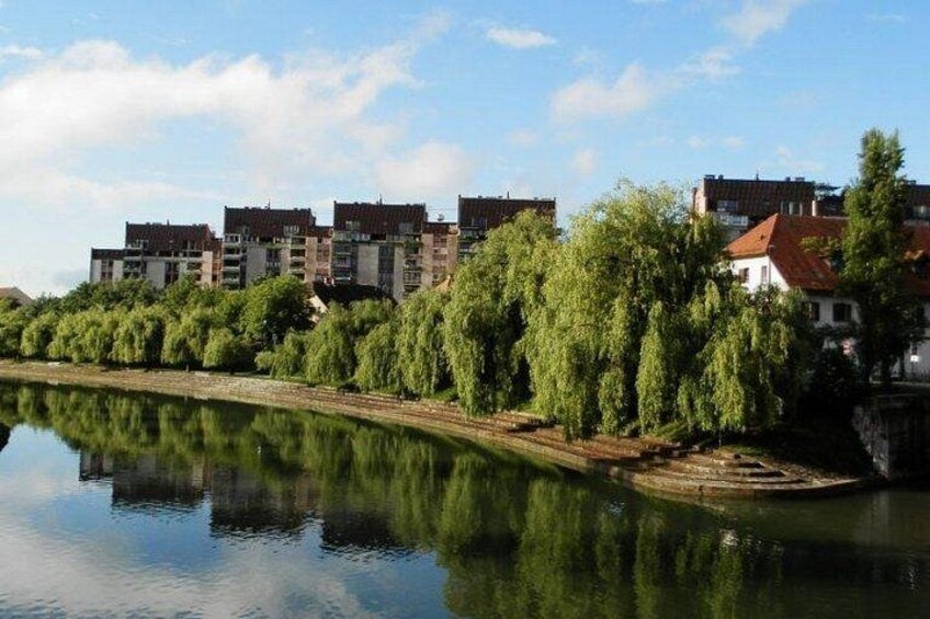 En stilla flod med speglingar i vattnet, en rad moderna byggnader och frodig grönska längs stränderna. 2