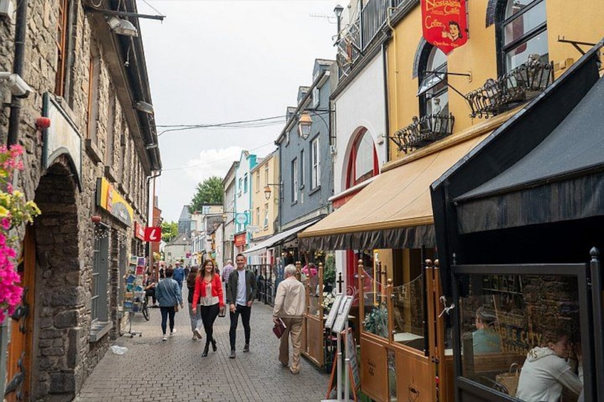 Una calle empedrada bordeada por edificios históricos, un café y gente caminando. 4