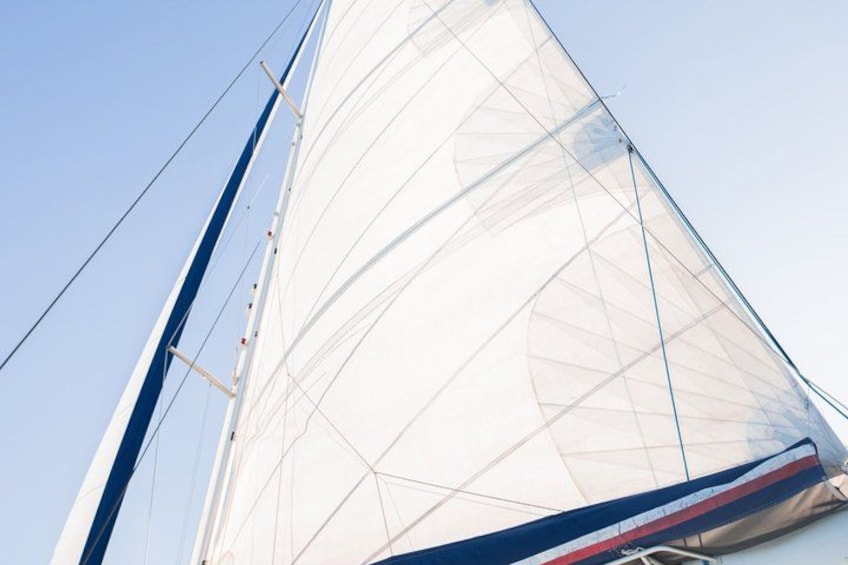 A sailboat with a large white sail and blue and red stripes. 2