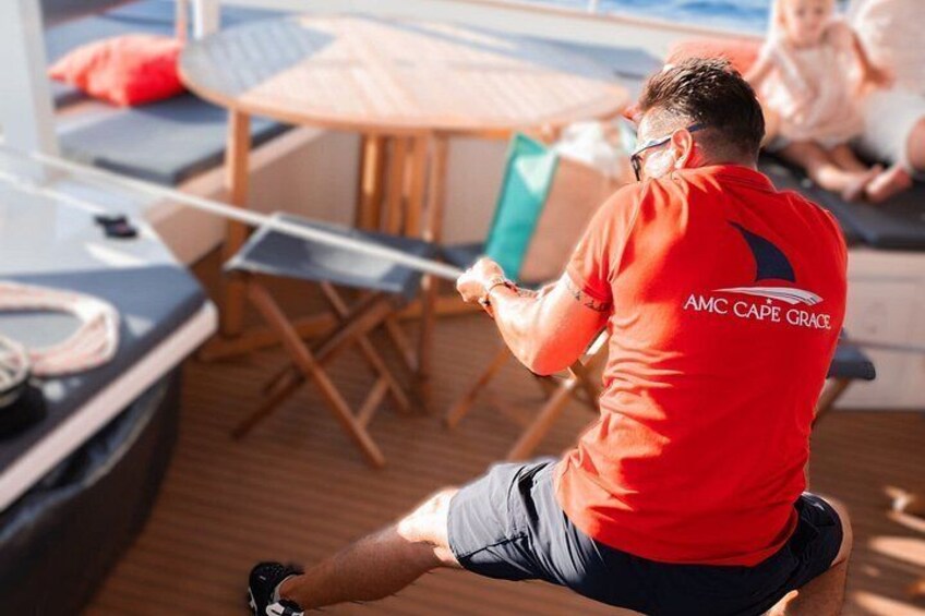 Una persona con una maglietta rossa con scritto 'AMC Cape Grace' sulla schiena, seduta su una sedia e che tiene una corda. 4