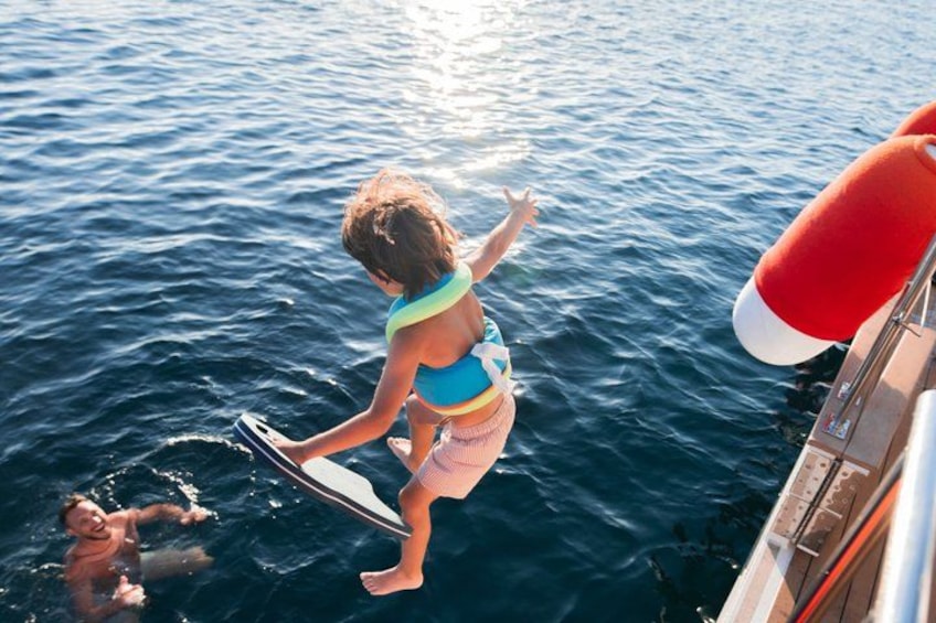 A person in a blue swimsuit and pink shorts standing on a boat, holding a board, with a red lifebuoy visible. 3