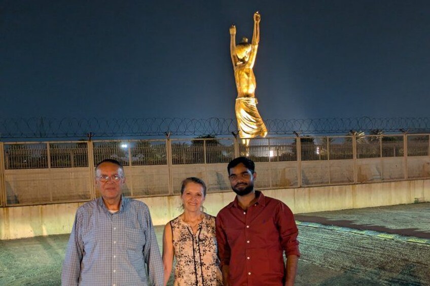 Drei Personen stehen vor einer goldenen Statue in der Nacht. 4