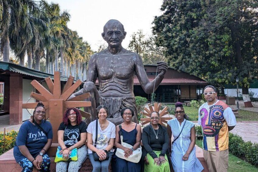 A group of people posing with a large statue and a decorative sun-like structure in a park. 5