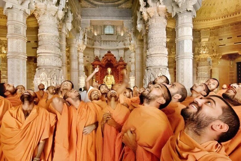 Monks in orange robes in a temple with ornate columns and a central statue. 3