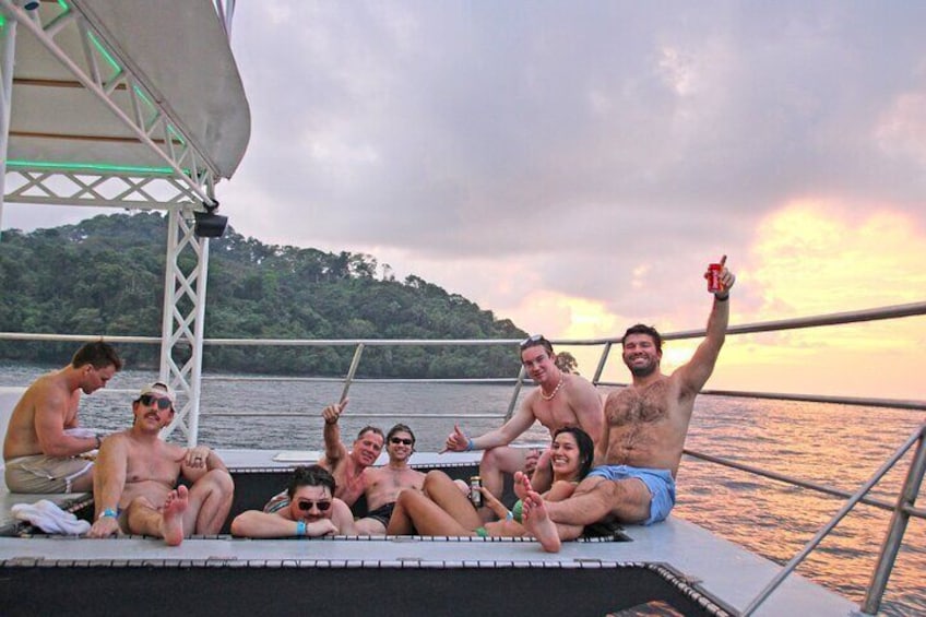 A group of people relaxing on a boat deck with a sunset in the background. 2
