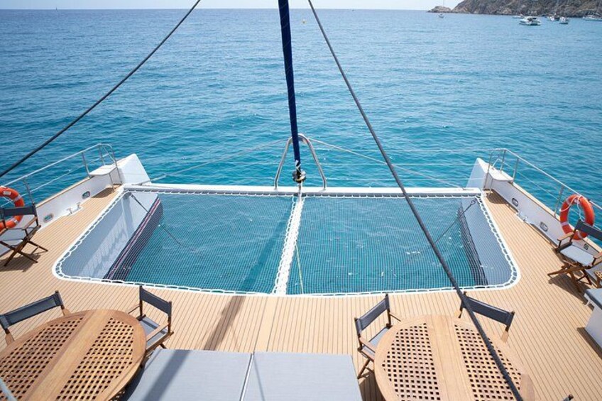 A boat deck with a netted swimming area, wooden flooring, and life rings. 3