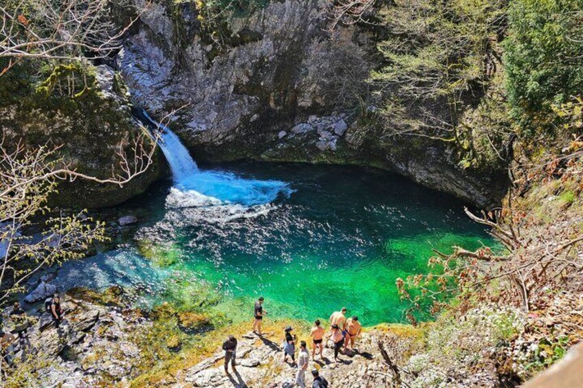 A waterfall in a rocky gorge with clear turquoise water, surrounded by trees and rocky terrain. 1
