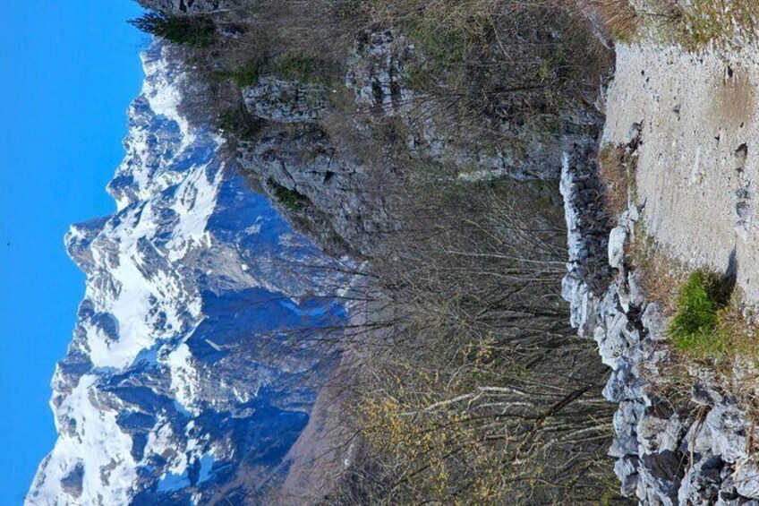 A mountainous landscape with snow-capped peaks, rocky cliffs, and sparse vegetation. 2