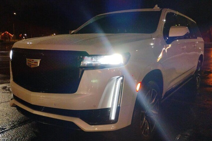 A white SUV with its headlights on, parked at night. 5