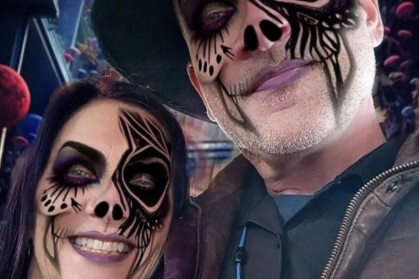 A person with a black and white face paint design, a leather jacket, and a black hat. 4