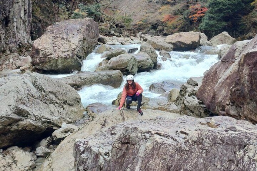 Une personne accroupie sur des rochers, près d’une rivière où l’eau coule et où l’on peut voir de gros blocs de pierre. 1