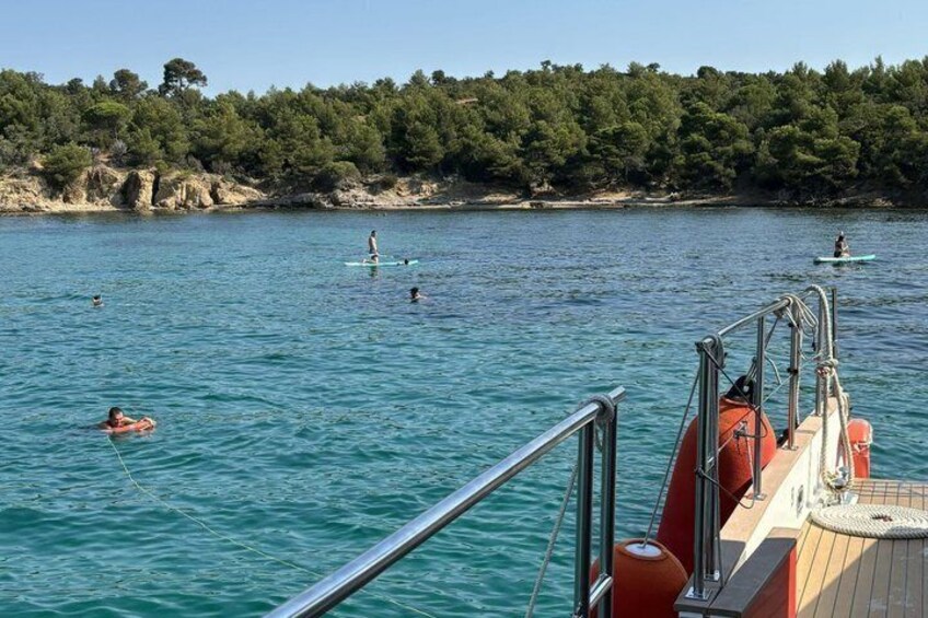 A calm sea with people swimming and paddleboarding, a boat deck with railings, and a forested coastline. 3