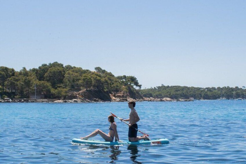 Two people on a paddleboard in a calm body of water with a forested coastline in the background. 1