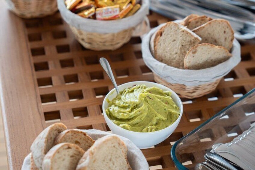 A table with a bowl of green spread, slices of bread, and baskets of snacks. 4