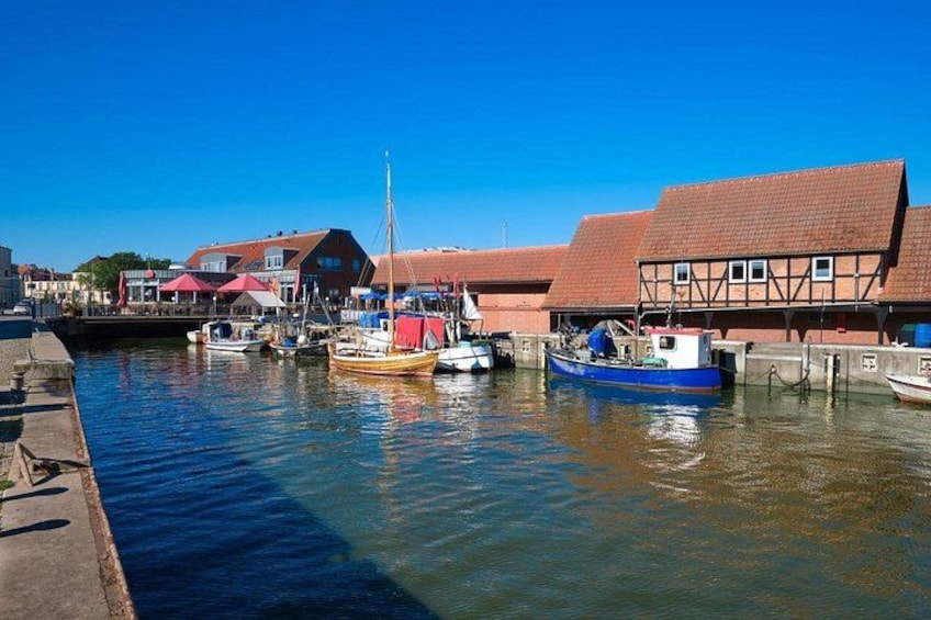 A harbor with boats docked, buildings with red roofs, and calm water reflecting the sky. 5