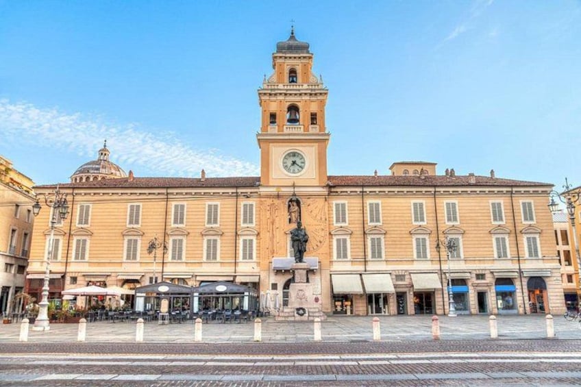 Un edificio storico con una torre dell'orologio, una statua di fronte e una piazza lastricata. 4