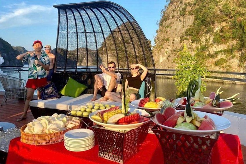 Un barco con zona de estar cubierta, una mesa con comida y bebidas, y un paisaje montañoso al fondo. 2