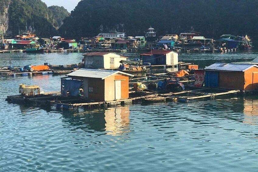 Un pueblo flotante con casas sobre pilotes, rodeado de barcos y un paisaje montañoso de fondo. 3