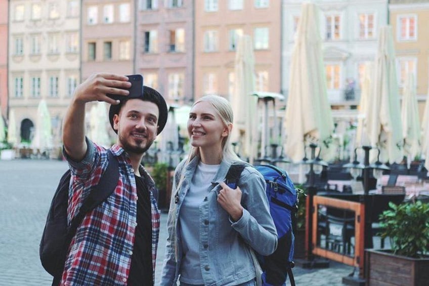 Zwei Personen machen ein Selfie vor einem historischen Gebäude in Europa, im Hintergrund befindet sich eine Terrasse. 2
